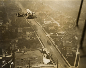 A single propellor plane flies over a residential neighborhood. The photograph was taken from another plane looking down on the other plane. 